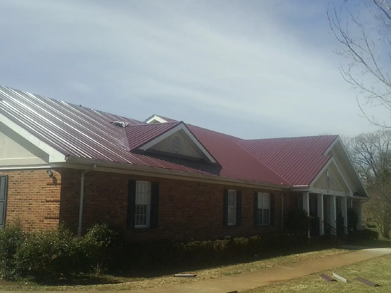 Red metal roof with gabled entries on a long brick building, from a Hail Damage Roof Repair job in Michie