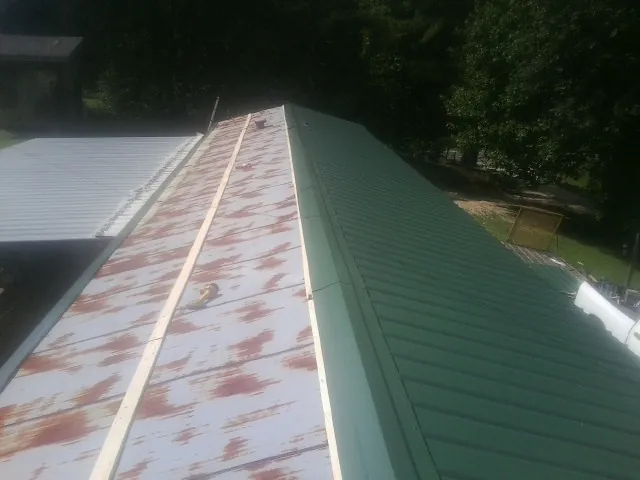 Old rusted panels beside newly installed green metal roofing — Wind Damage Roof Repair by Roofing Brothers in Michie