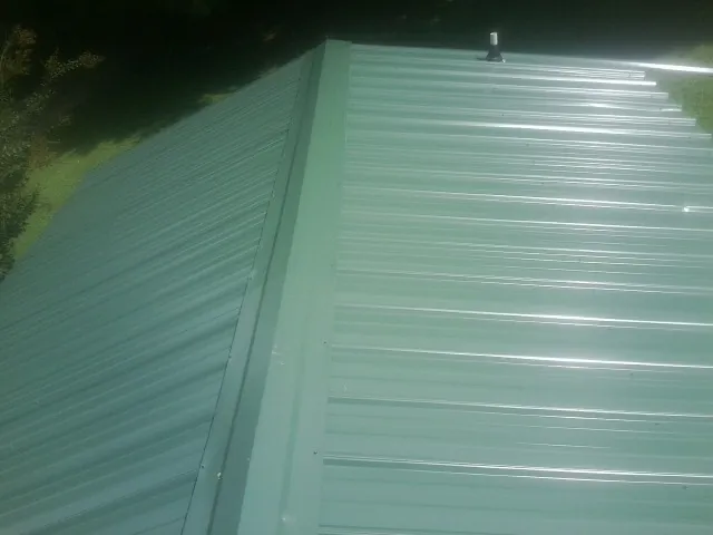 New green metal panels meeting at the ridge of a roof — Flat Roof Repair work by our crew in Michie