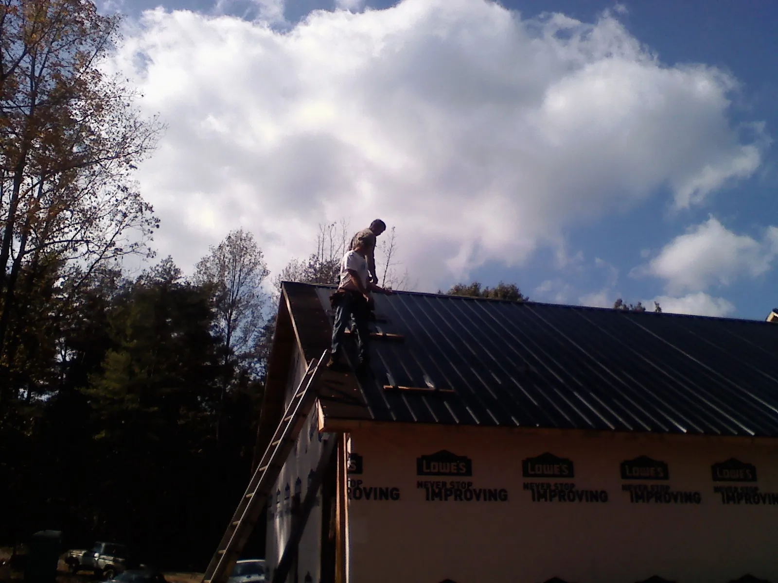 Roofer fastening dark metal panels high against a cloudy sky, from a Roof Inspection job in Michie