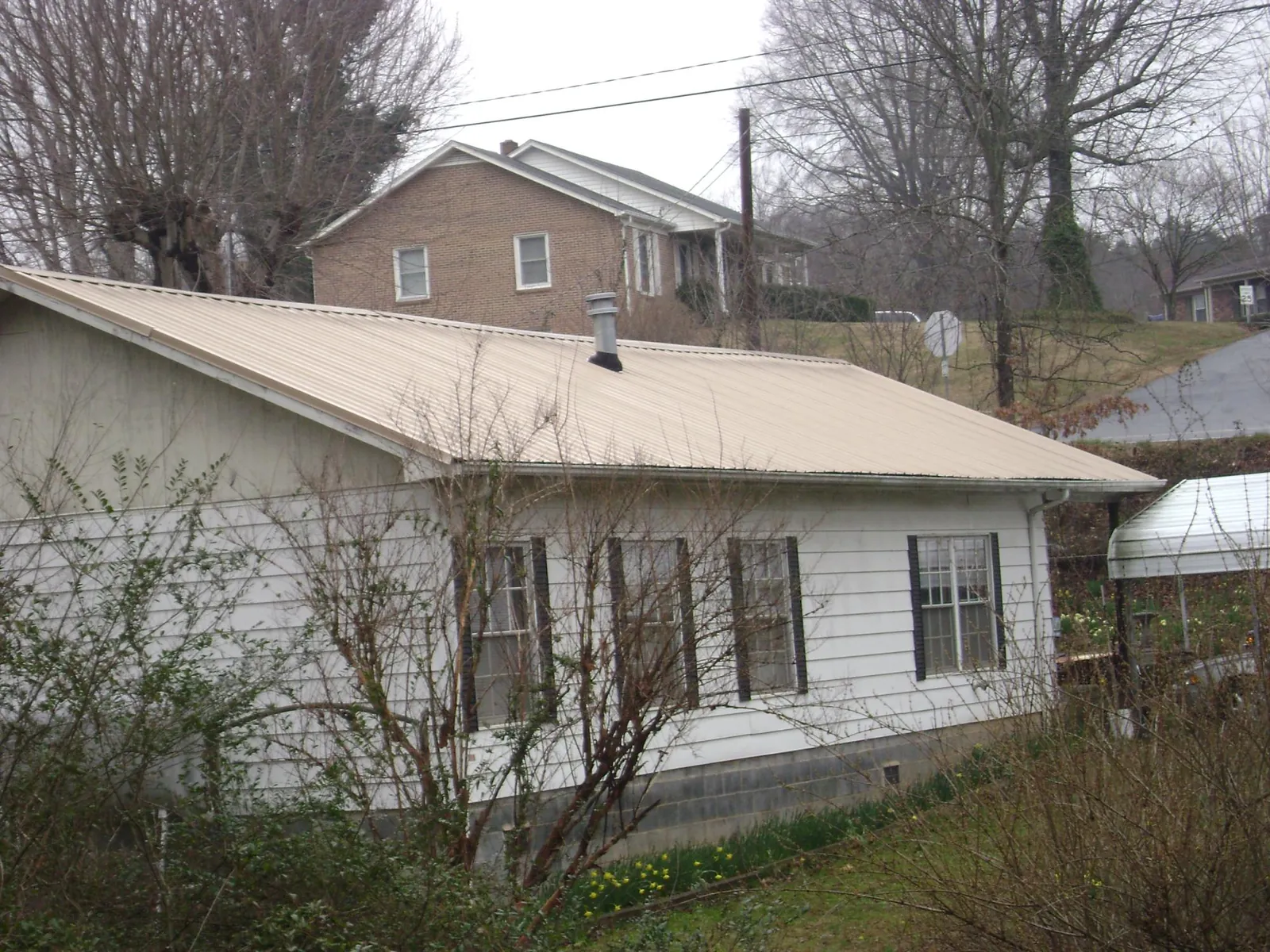 Tan metal roof on a white sided house set into a hillside — Commercial Roofing by Roofing Brothers in Michie