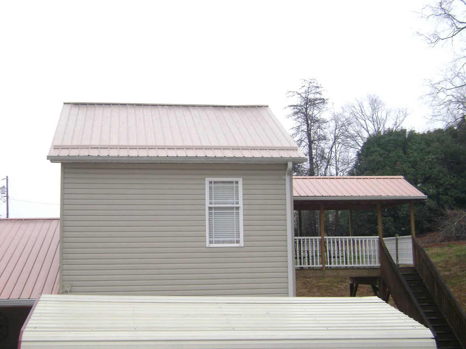 Tan metal roofs on a two story addition and attached porch, from a Roof Replacement job in Michie